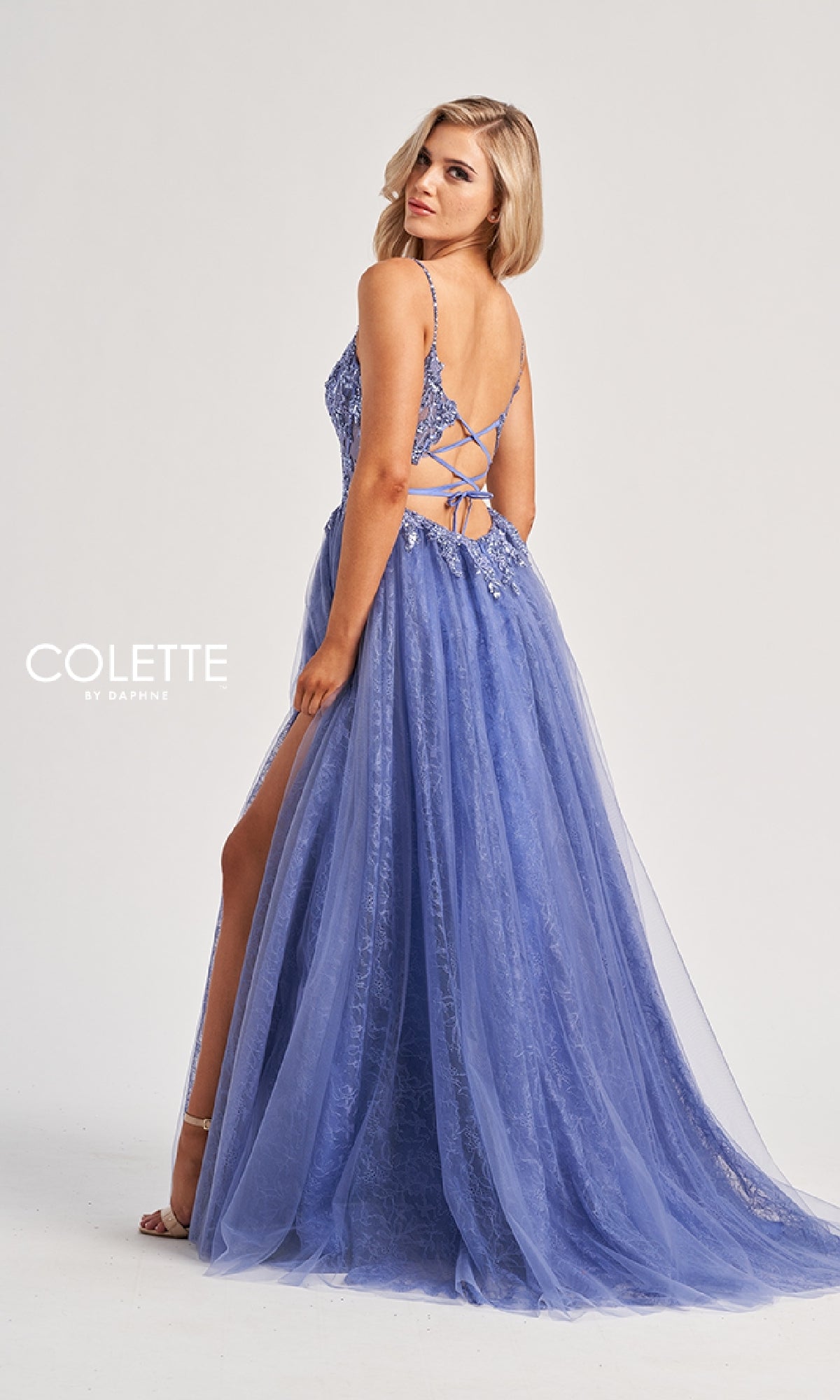 A woman models the Colette CL8240 long prom dress with a lavender lace design, embroidered bodice, spaghetti straps, and open back, posing against a plain white background.